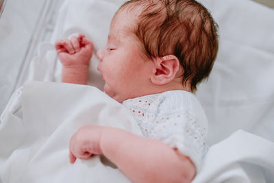 From above of adorable newborn child with dark hair sleeping in bed with white sheets