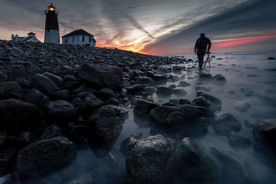 Man standing on rock against sky during sunset