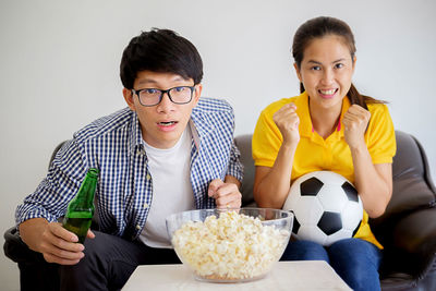 Portrait of friends cheering while sitting on sofa at home