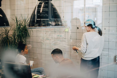 Multi-ethnic hackers discussing over wall at creative office seen through window