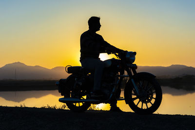 Silhouette man riding motorcycle on mountain against sky during sunset