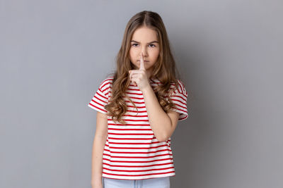 Portrait of young woman standing against gray background