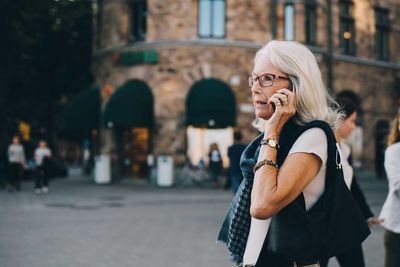 Senior woman talking through smart phone while looking away in city