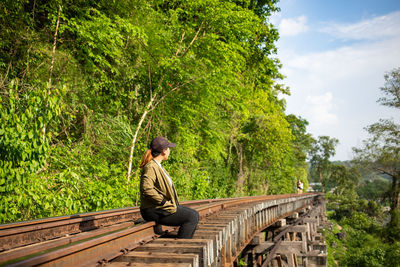 Woman sitting by trees on railroad track