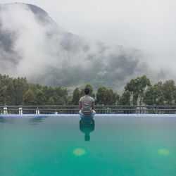 Rear view of man looking at swimming pool against lake
