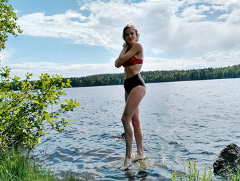 Portrait of smiling young woman standing in lake against sky