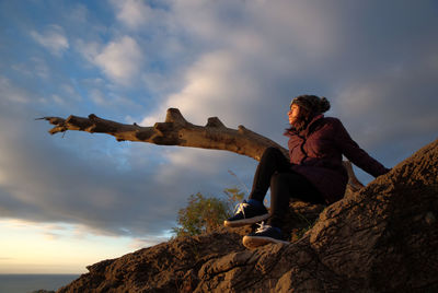 Low angle view of woman sitting on rock against sky