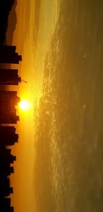 Silhouette buildings by sea against sky during sunset