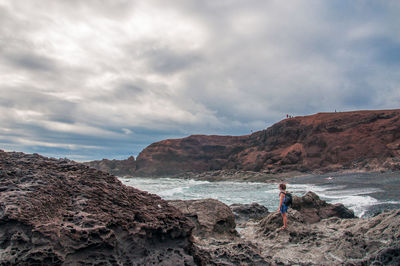 Man standing on rock by sea against sky