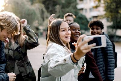 Happy multi-ethnic friends taking selfie with mobile phone on street in city