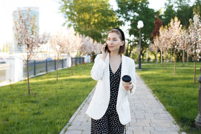 Smiling woman talking on phone while standing on footpath