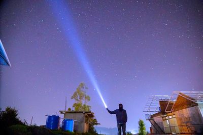 Rear view of man standing on building against sky at night