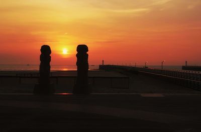 Silhouette people standing against orange sky during sunset