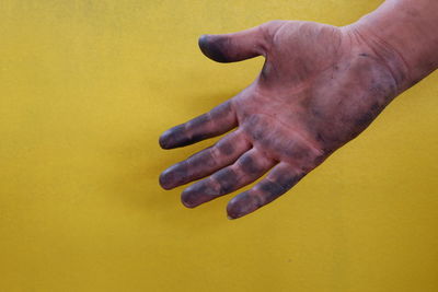 Close-up of dirty hand against yellow background