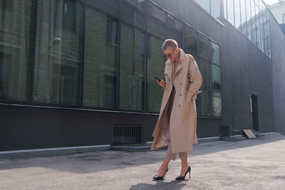 Full length of woman using mobile while standing against building