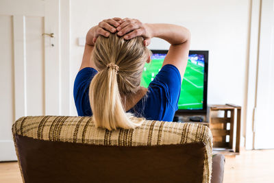 Rear view of woman watching soccer match on television set in living room at home