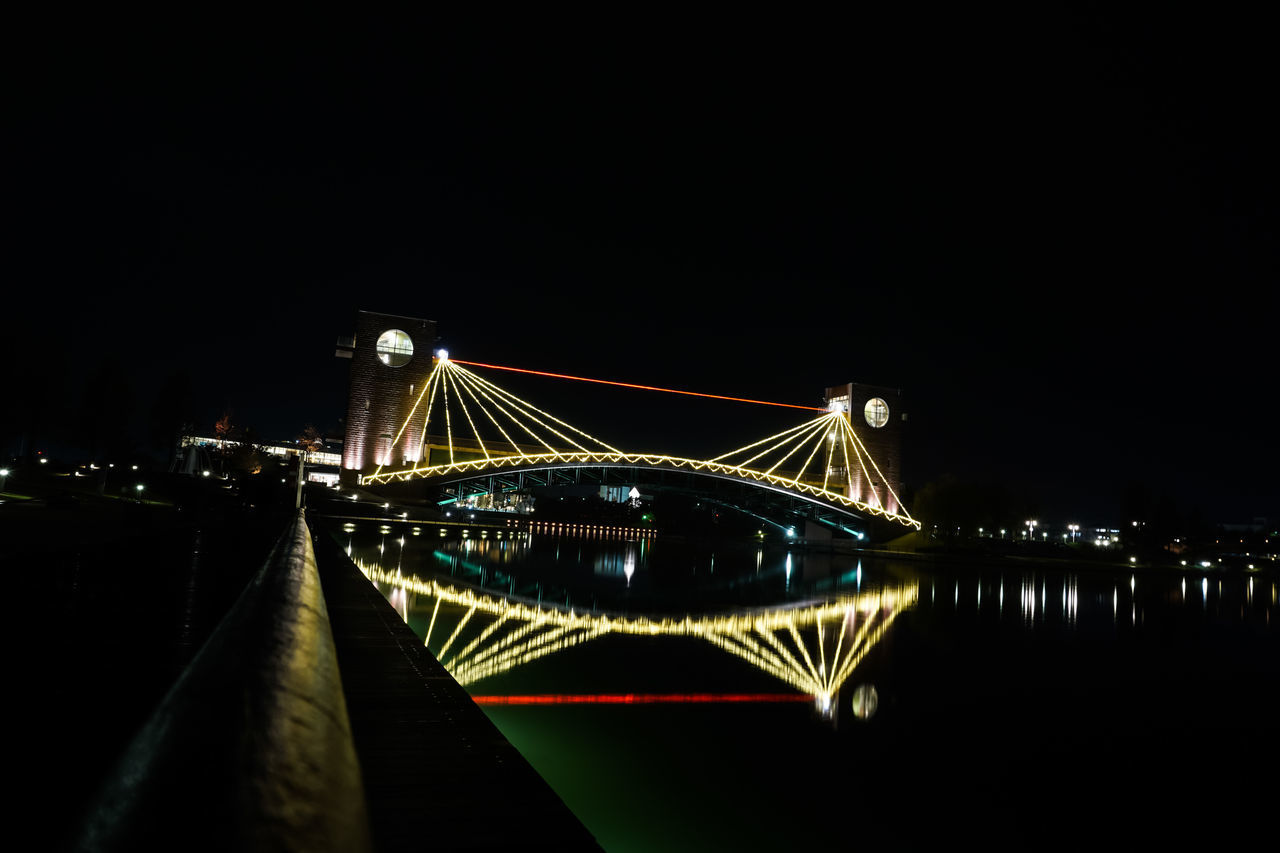 ILLUMINATED BRIDGE OVER RIVER AGAINST SKY