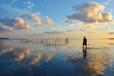 Silhouette man standing in sea against sky during sunset