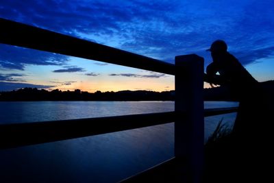 Silhouette man standing by railing against sky during sunset