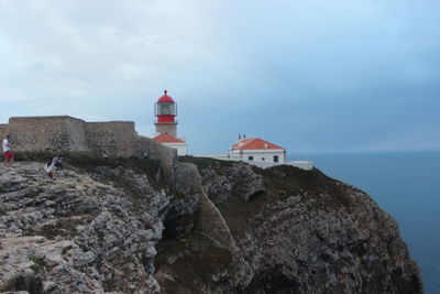 Lighthouse by sea and buildings against sky