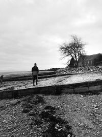 Rear view of man walking on beach against sky