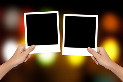 Close-up of hand holding photographs over illuminated background