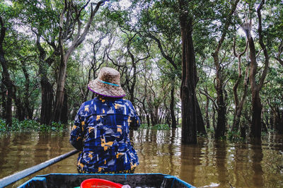 Rear view of woman sitting by lake in forest