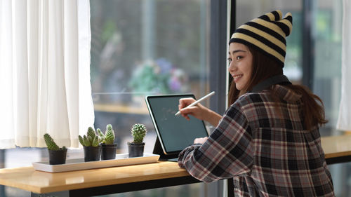 Young woman using phone while standing by window