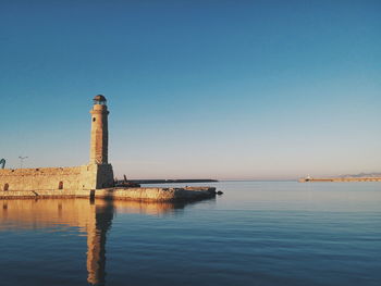 Lighthouse by sea against blue sky