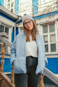 Portrait of young woman standing against building