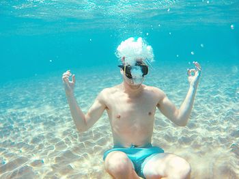 Shirtless young man wearing swimming goggles while swimming undersea