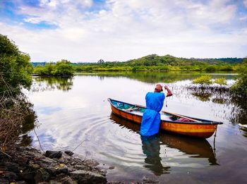 Rear view of man on boat in lake against sky