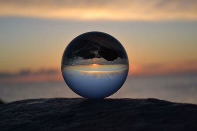 Close-up of crystal ball against sea during sunset