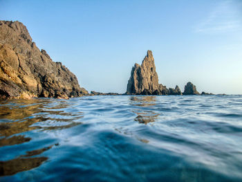 Rock formations in sea against clear blue sky