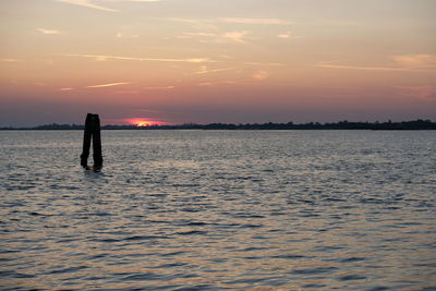 Silhouette people standing on sea against sky during sunset