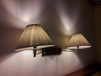 Illuminated lamp on table against wall at home