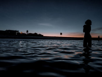 Silhouette man standing in sea against sky during sunset