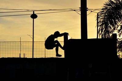 Silhouette boy climbing on wall against sky during sunset