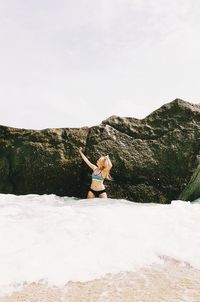 Woman enjoying by rock at beach against sky
