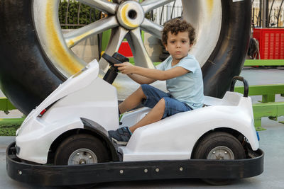 Beautiful curly-haired caucasian boy sitting in electric car, looking at the camera