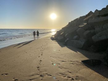 People on beach against sky during sunset