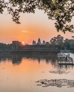 Scenic view of river by buildings against sky during sunset