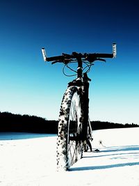 Bicycle on snow covered land against clear blue sky