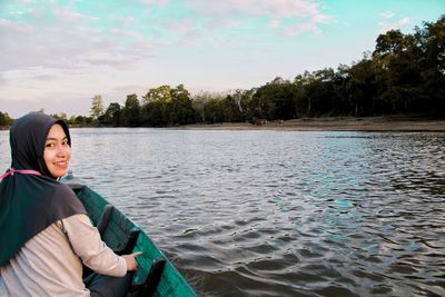 Portrait of smiling young woman by lake against sky