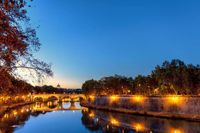 Illuminated bridge over river against clear sky during dusk