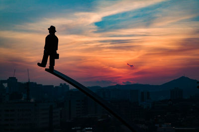 Silhouette of statue in city against cloudy sky during sunset