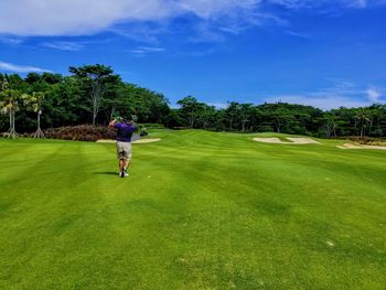 Rear view of man playing golf on course against sky