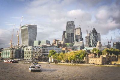 Modern buildings by river against sky in city