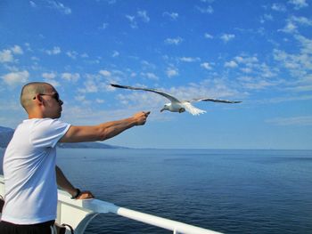 Young man flying bird by sea against sky