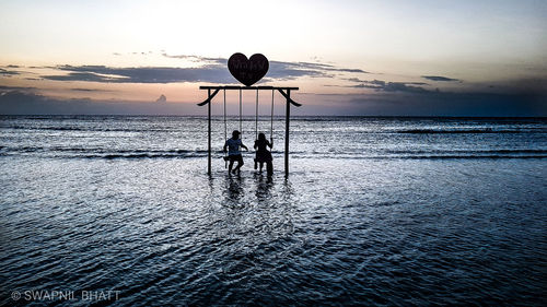 Silhouette people on beach against sky during sunset